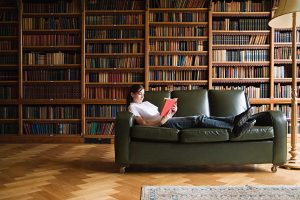 A book collector reads a treasured book on a couch in her library of bookshelves